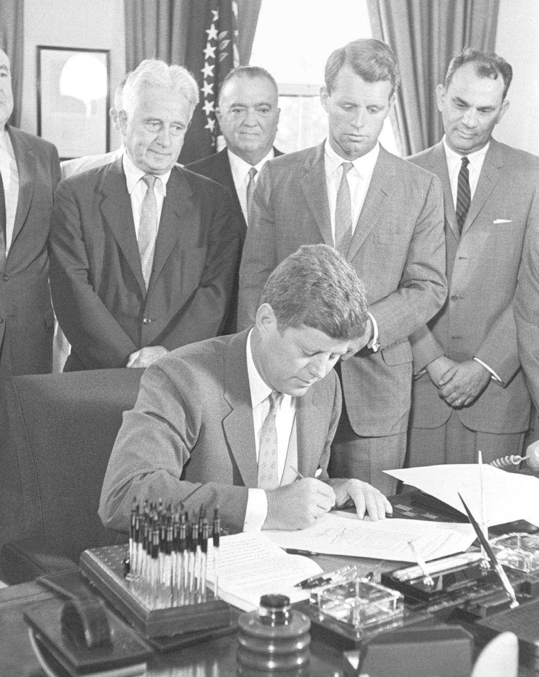 President John F. Kennedy signs antiracketeering bills while Senator Kenneth B. Keating, FBI Director J. Edgar Hoover, and Attorney General Robert F. Kennedy look on, Washington, DC, 1961.