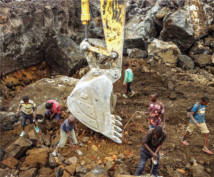 Children collect pieces of metal scrap to sell while a backhoe clears boulders from a construction site, Goma, Congo, 2013.